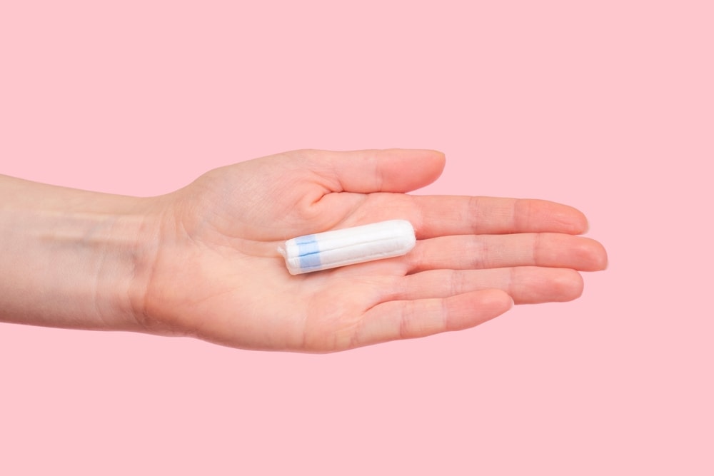 single tampon in human hand pink background