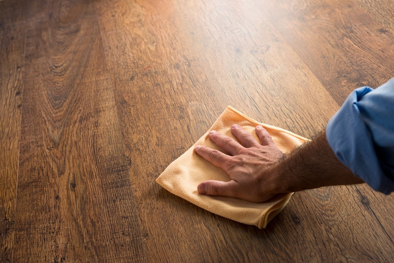 Male hand cleaning and rubbing an hardwood floor with a microfiber cloth.