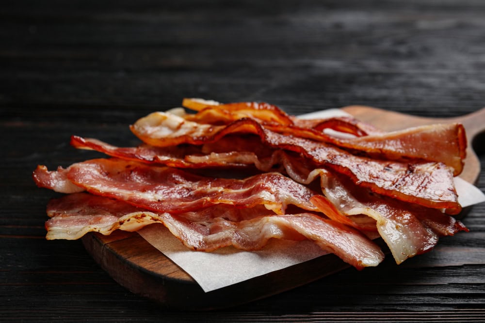 Slices of tasty fried bacon on black wooden table
