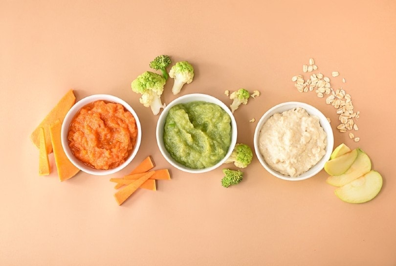 3 platos de comida para bebé con algunos vegetales en la mesa.