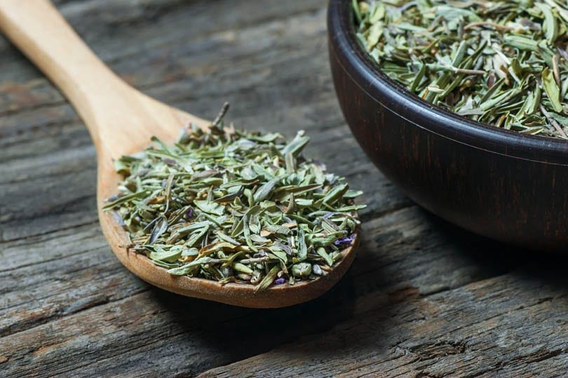 heap of dry thyme in wooden spoon and in bowl on wooden background