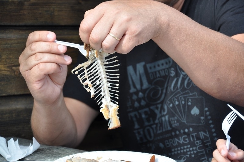 man eating whole fish with bones