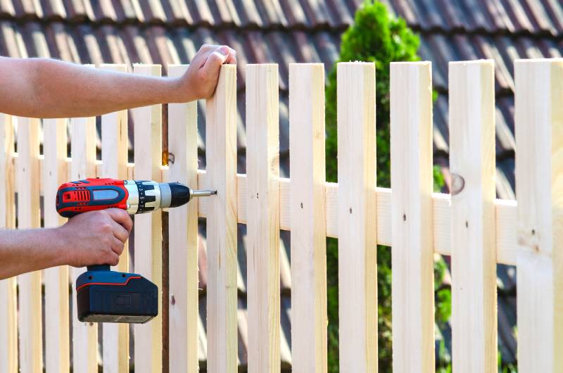 người đàn ông xây hàng rào gỗ bằng máy khoan và vít