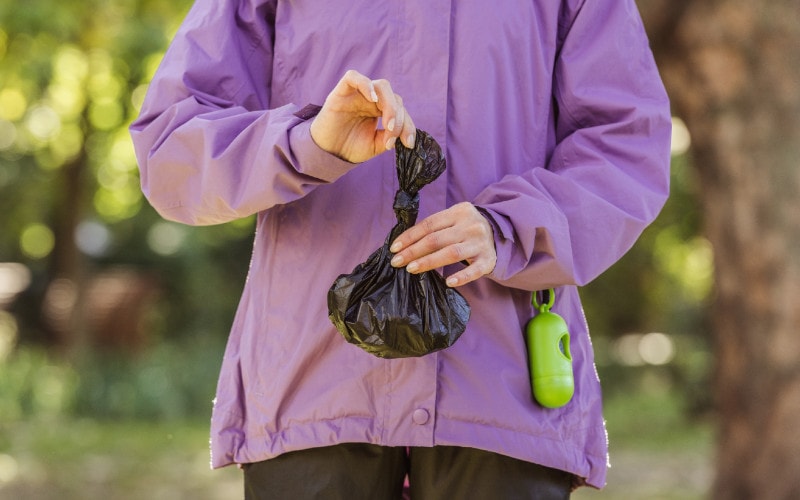 woman holding trash bag after cleaning up dog poop outdoors