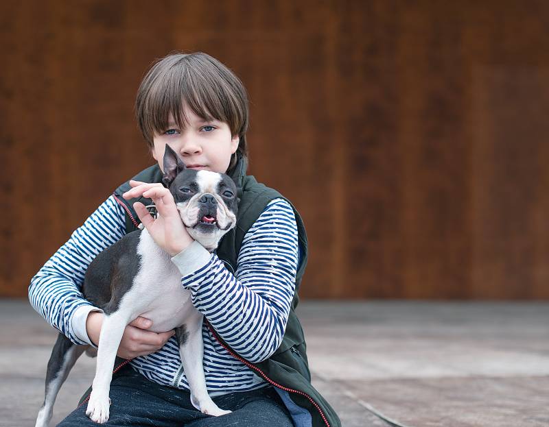 boy holding and hugging a boston terrier dog