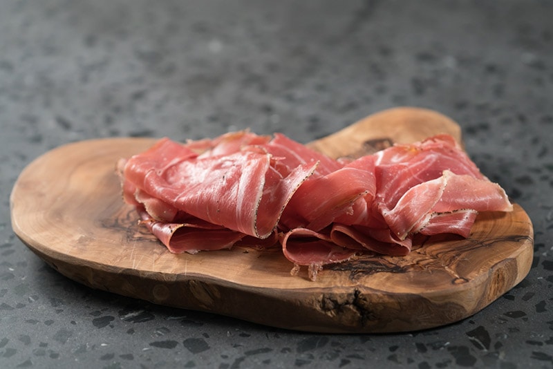 sliced prosciutto ham on wooded board