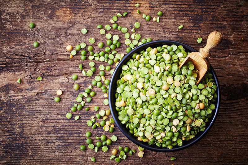 Bowl of green split peas on wooden background