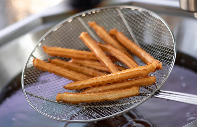 freshly deep fried churros on a stainless steel strainer