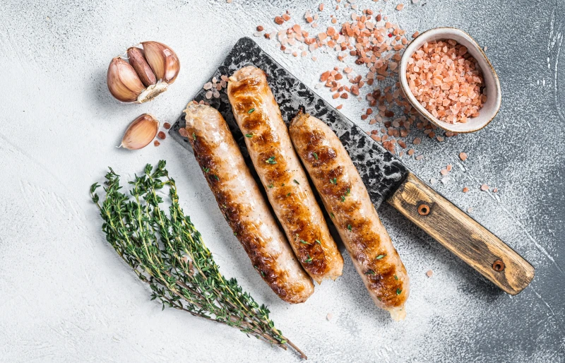 xúc xích bratwurst nướng trên dao phay với tỏi, muối và lá hương thảo