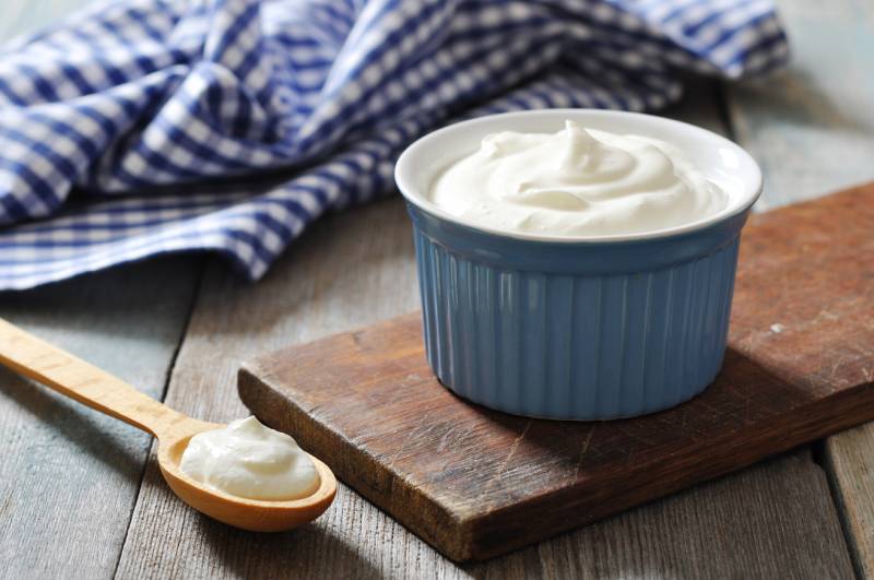 Greek yogurt in a ceramic bowl with spoons on wooden background