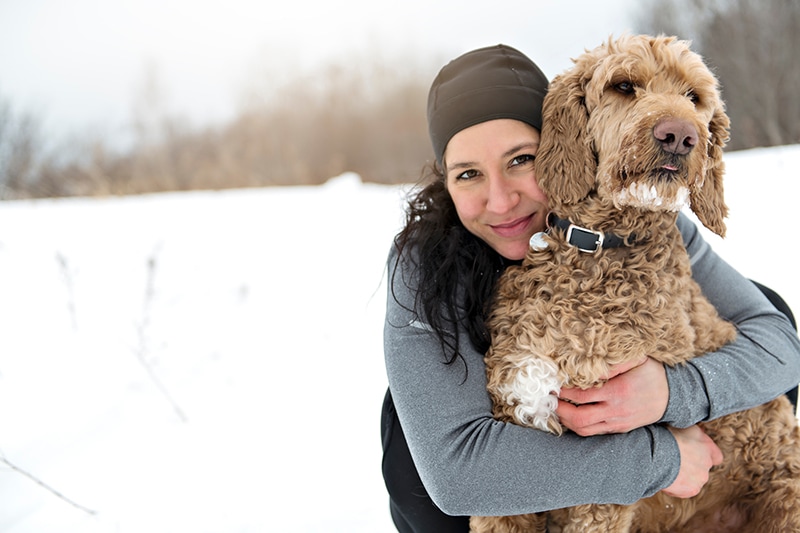 Woman hugging her goldendoodle dog outdoor during winter