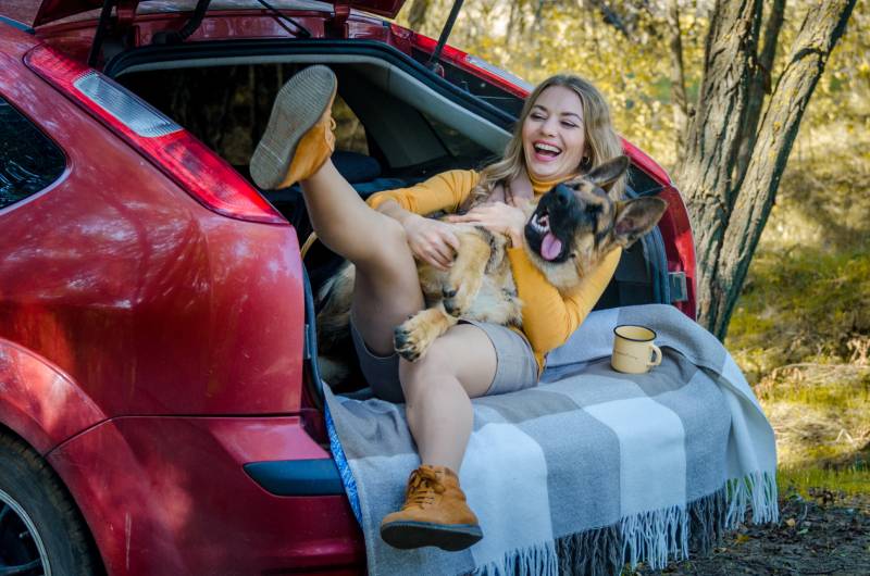 young owner laughing with her dog at the back of the car