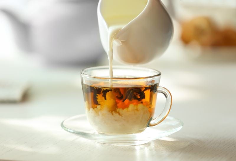 Pouring milk in tea on table