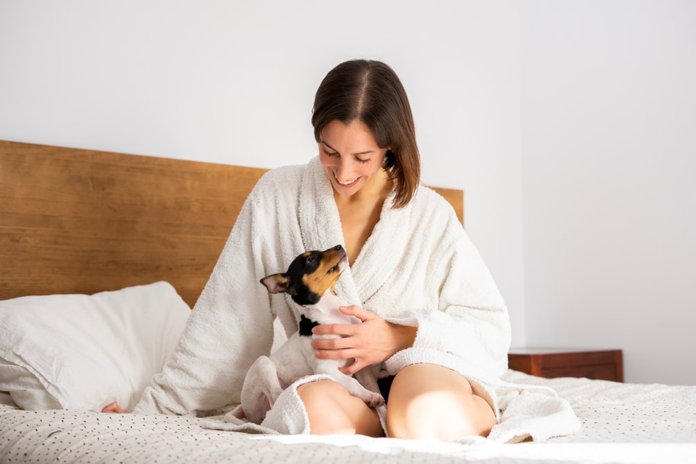 Woman dog owner in bathrobe on a bed with her dog