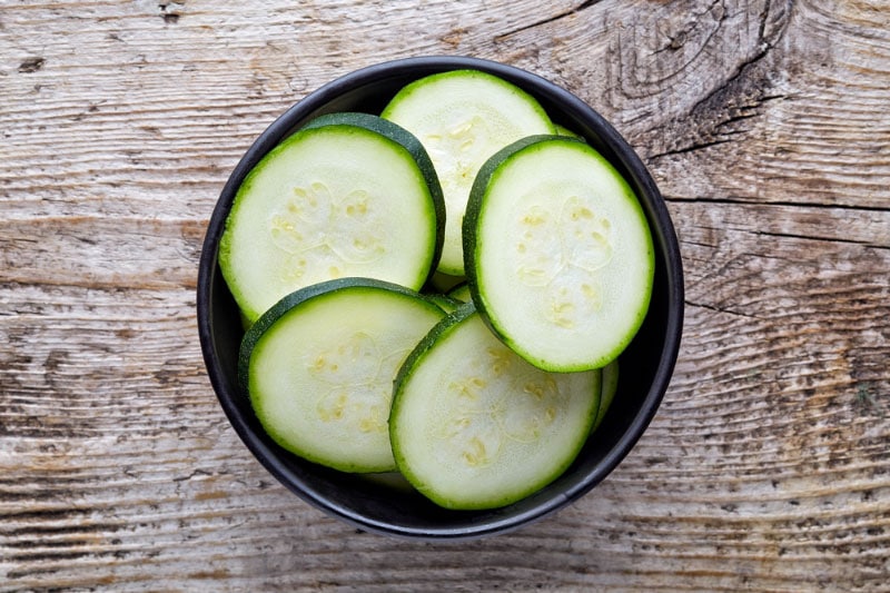 bowl of fresh zucchini slices on wooden background