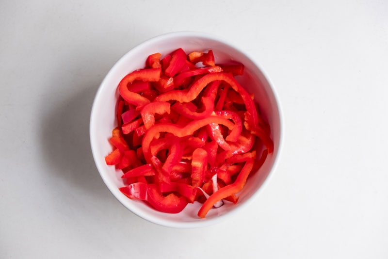 top view of sliced red bell peppers in white bowl