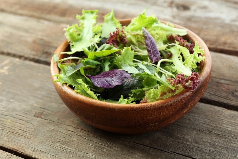 a bowl of spring mix on wooden surface
