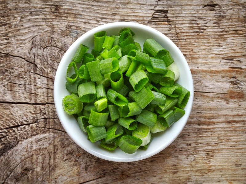 bowl of chopped green onions on wooden table