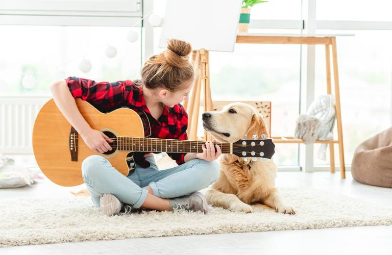 teenage girl playing guitar with lovely dog indoors