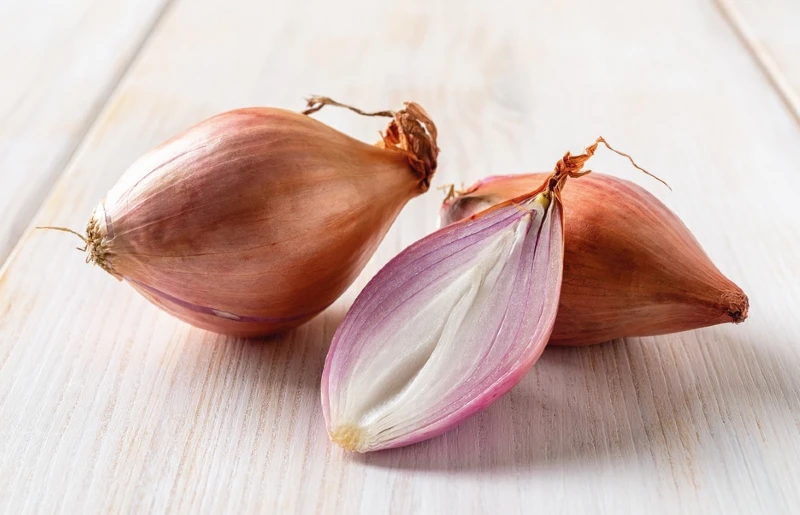 whole and half red shallots on a wooden surface