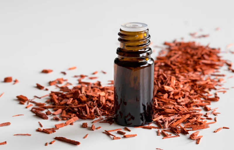 a bottle of sandalwood essential oil with sandalwood chips on white surface