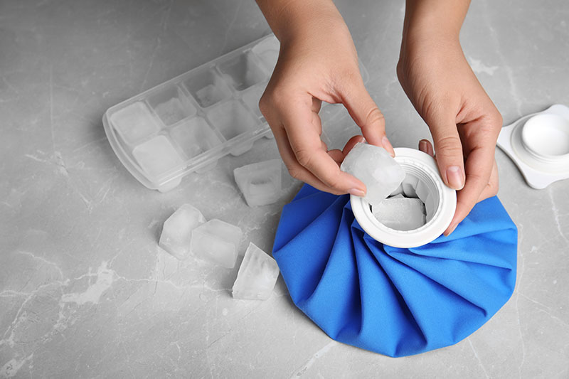 Woman putting ice cubes into pack at marble table