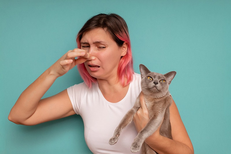 woman covering her nose because of the smelly cat