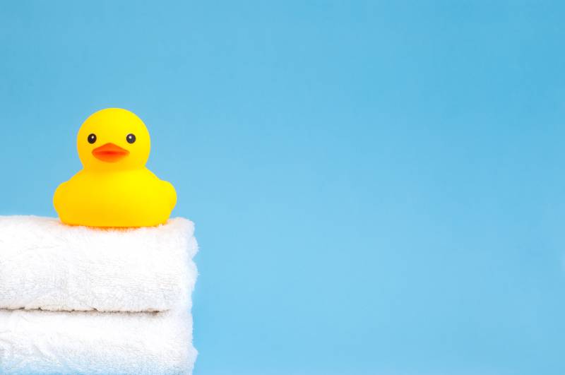 Yellow duck squeaker bath toy on a white towel stack and blue background