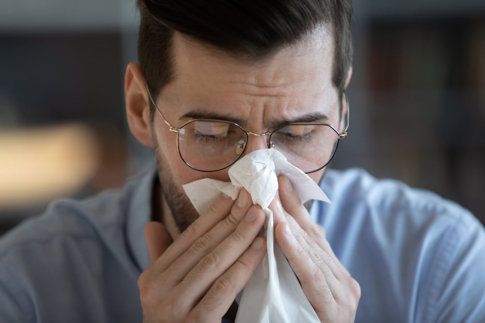 man holding tissue and sneezing, blowing runny nose, sick, allergy